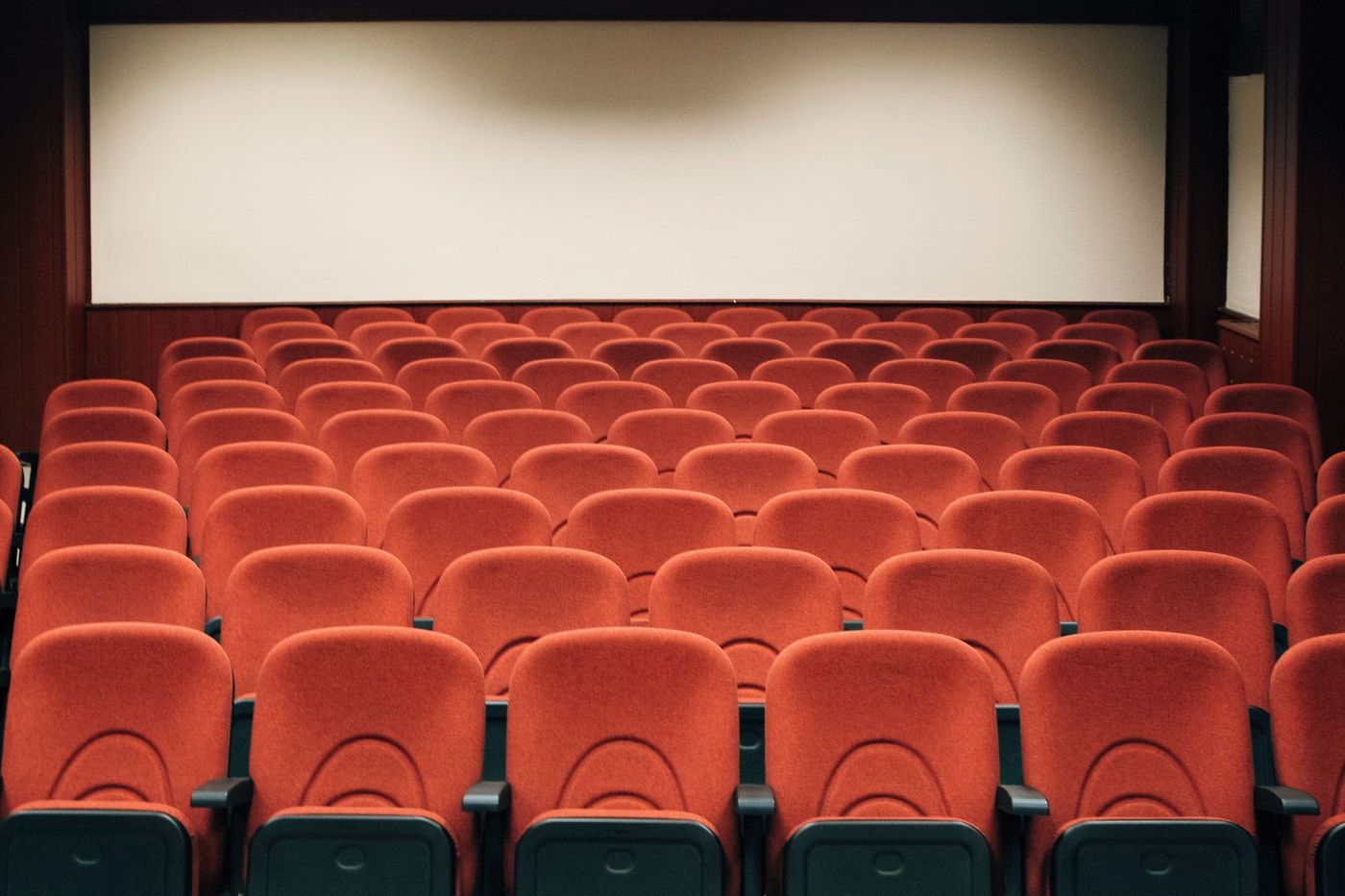 Rows of empty red cinema seats facing a blank screen