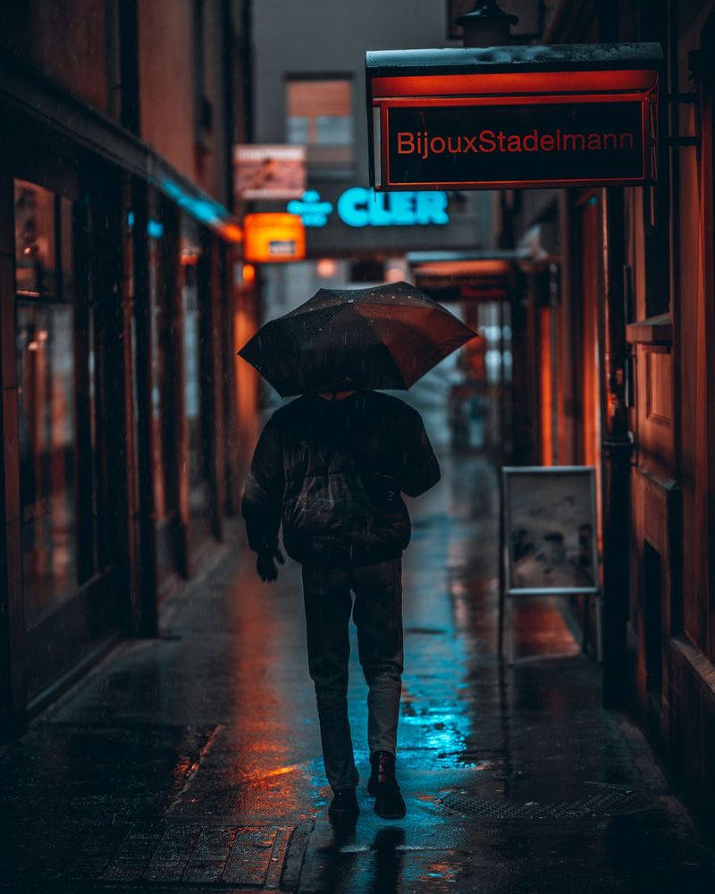 A figure with an umbrella in a neon-lit rainy alley